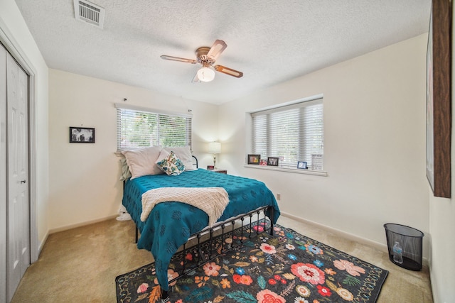 carpeted bedroom with visible vents, baseboards, a ceiling fan, and a textured ceiling