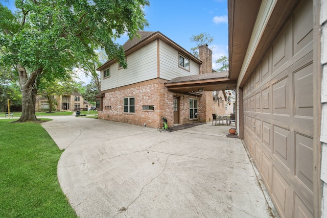 view of home's exterior featuring a lawn, a patio area, brick siding, a chimney, and concrete driveway