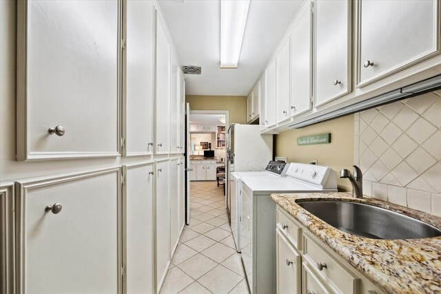 clothes washing area featuring light tile patterned floors, independent washer and dryer, visible vents, a sink, and cabinet space