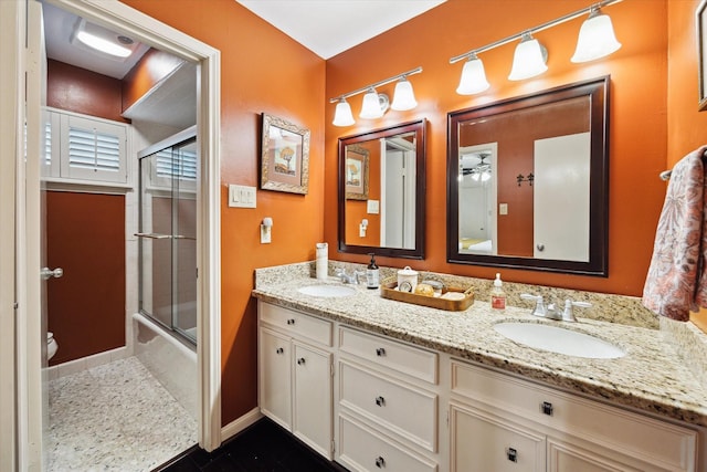 full bath featuring bath / shower combo with glass door, double vanity, a sink, and toilet