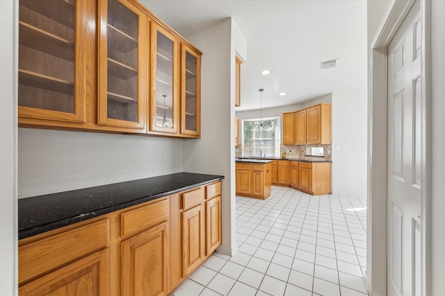 kitchen featuring light tile patterned floors, glass insert cabinets, visible vents, dark stone counters, and hanging light fixtures