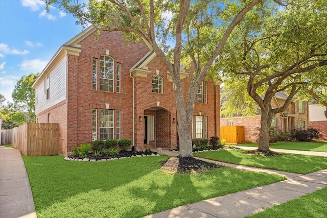 traditional-style house with brick siding, a front lawn, and fence