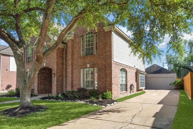 view of front of property featuring a detached garage, a front yard, brick siding, an outbuilding, and fence