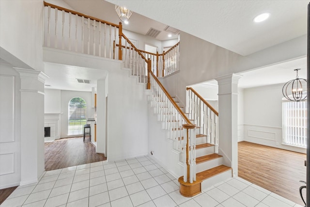 staircase featuring visible vents, a notable chandelier, a decorative wall, decorative columns, and tile patterned flooring