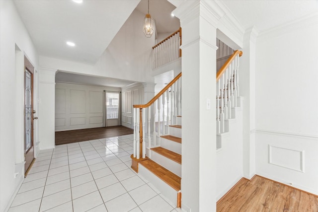 tiled foyer with a decorative wall, stairway, a high ceiling, and crown molding