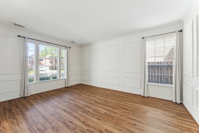 empty room featuring a decorative wall, visible vents, light wood finished floors, and ornamental molding