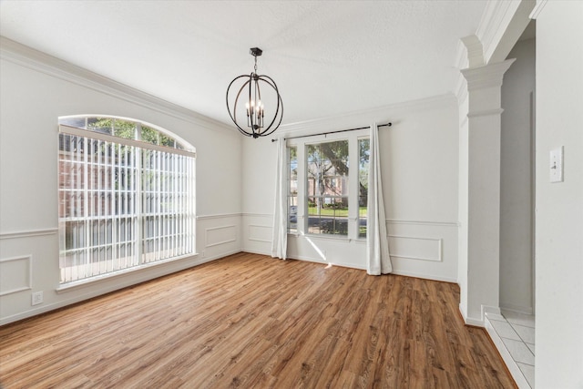 unfurnished dining area featuring ornamental molding, plenty of natural light, a chandelier, and wood finished floors