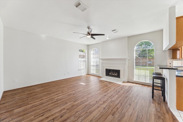 unfurnished living room with visible vents, baseboards, a tiled fireplace, a ceiling fan, and wood finished floors