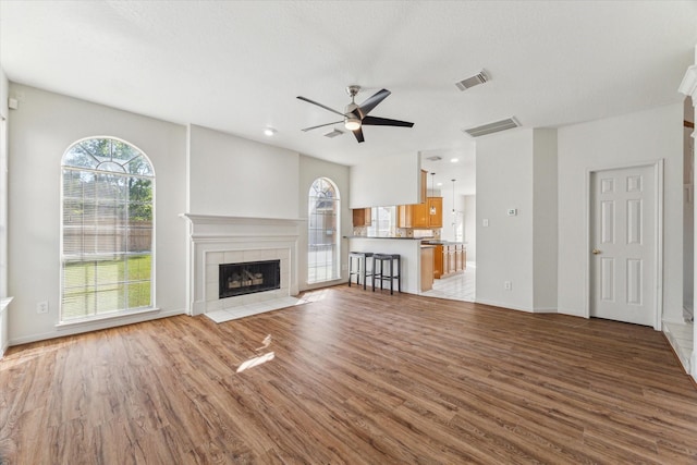 unfurnished living room with visible vents, a ceiling fan, a tile fireplace, and wood finished floors