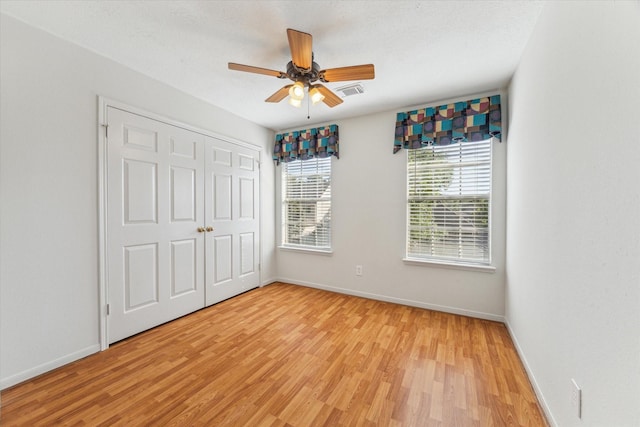 unfurnished bedroom featuring ceiling fan, light wood-type flooring, a closet, visible vents, and baseboards