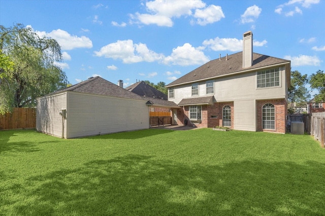 back of house featuring a lawn, a chimney, a fenced backyard, an outdoor structure, and brick siding