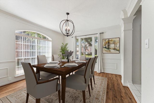 dining room with decorative columns, wood finished floors, ornamental molding, and an inviting chandelier