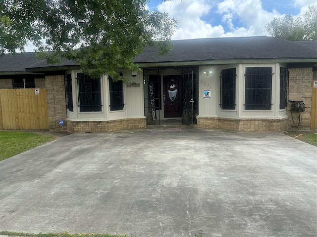 view of front facade featuring fence, a shingled roof, and brick siding