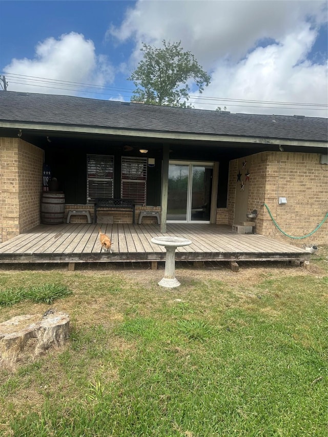 rear view of property with a lawn, brick siding, a wooden deck, and roof with shingles