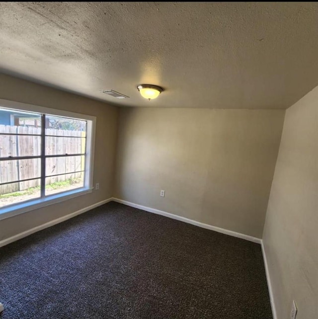 unfurnished room with dark colored carpet, visible vents, a textured ceiling, and baseboards