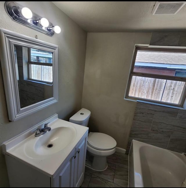 full bath featuring visible vents, a bathing tub, toilet, vanity, and marble finish floor