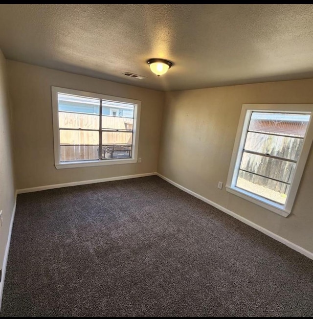 spare room with a textured ceiling and dark colored carpet