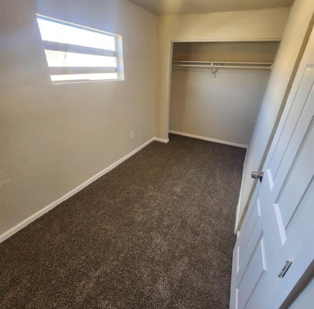 unfurnished bedroom featuring dark carpet, baseboards, and a closet