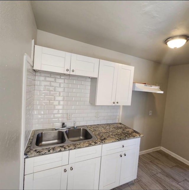 kitchen featuring tasteful backsplash, baseboards, light stone counters, white cabinets, and a sink