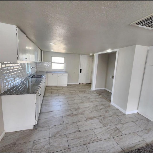 kitchen featuring baseboards, a textured ceiling, a sink, and visible vents