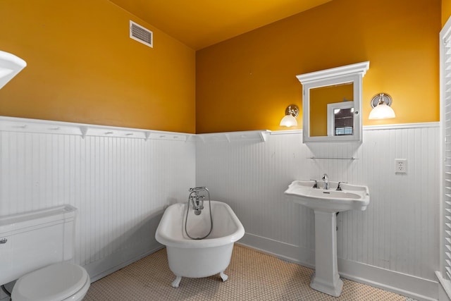 full bathroom featuring a soaking tub, tile patterned floors, toilet, a wainscoted wall, and visible vents