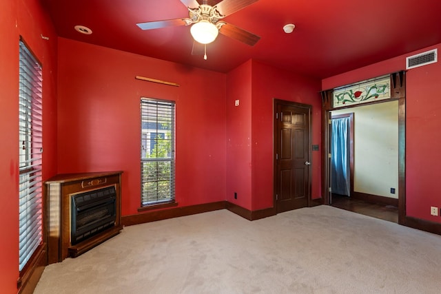 unfurnished living room with a glass covered fireplace, a ceiling fan, visible vents, carpet floors, and baseboards