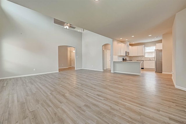 unfurnished living room with baseboards, recessed lighting, light wood-style flooring, ceiling fan, and arched walkways
