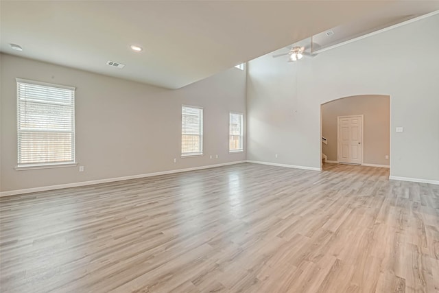 empty room with arched walkways, baseboards, a ceiling fan, and light wood-style floors