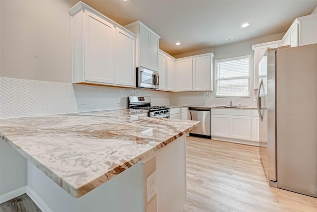 kitchen featuring a peninsula, white cabinets, stainless steel appliances, light wood finished floors, and a sink