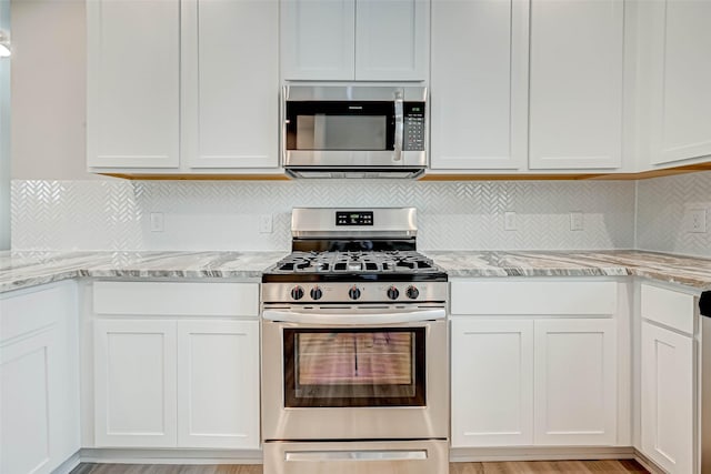kitchen with white cabinets, appliances with stainless steel finishes, and light stone counters