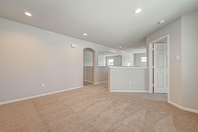 spare room featuring light carpet, recessed lighting, baseboards, and arched walkways