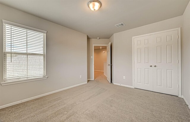 unfurnished bedroom with light carpet, a closet, baseboards, and visible vents