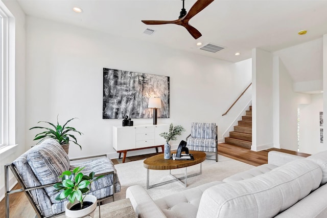 living room featuring stairs, visible vents, wood finished floors, and ceiling fan