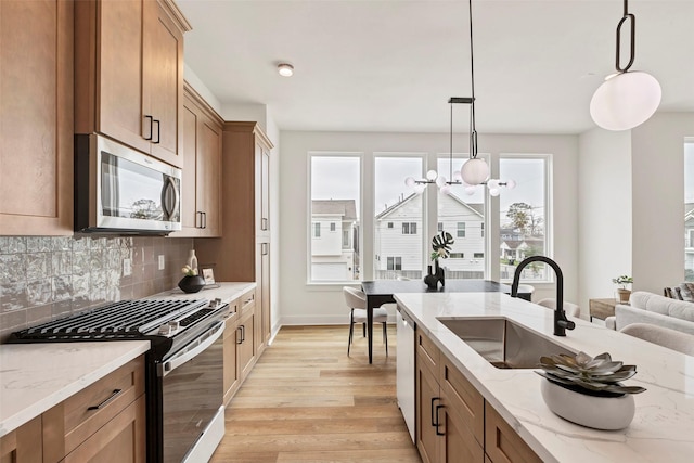 kitchen featuring decorative light fixtures, a sink, light wood-style floors, stainless steel appliances, and backsplash