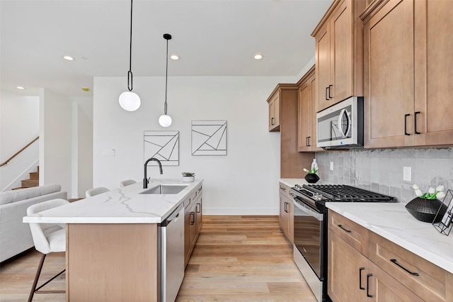 kitchen featuring a sink, light wood finished floors, stainless steel appliances, backsplash, and a breakfast bar area