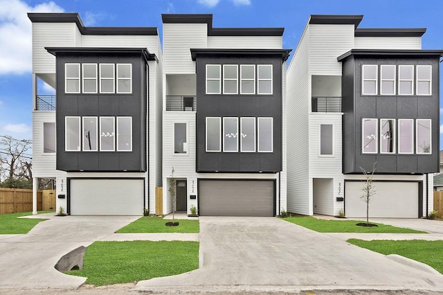 view of front of house featuring an attached garage, driveway, fence, and a balcony