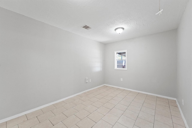 empty room with a textured ceiling, light tile patterned flooring, baseboards, and visible vents
