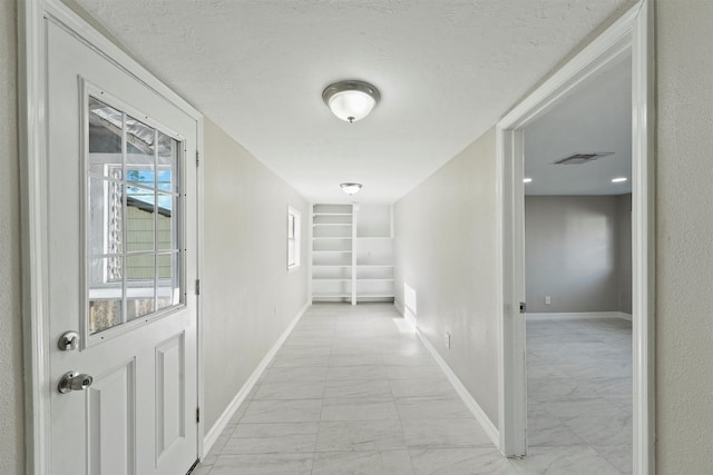 hall with visible vents, marble finish floor, baseboards, and a textured ceiling