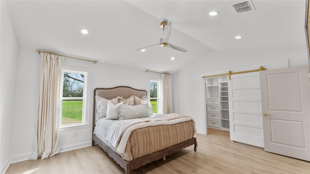 bedroom featuring light wood-type flooring, a spacious closet, visible vents, lofted ceiling, and baseboards
