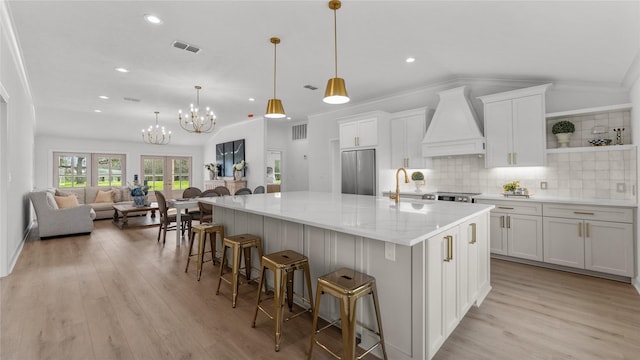 kitchen featuring an inviting chandelier, light wood-type flooring, white cabinetry, custom exhaust hood, and stainless steel fridge