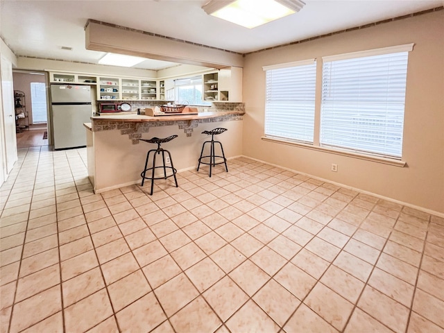 3203 Bayou Dr, La Porte, TX 77571 - kitchen featuring freestanding refrigerator, a peninsula, open shelves, a breakfast bar area, and light tile patterned floors