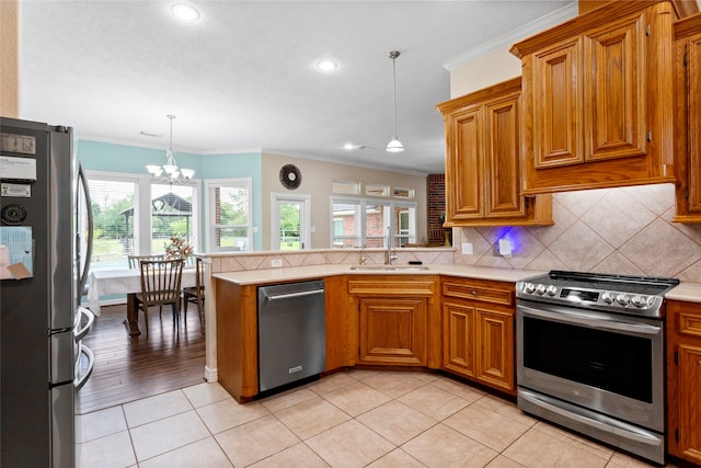 kitchen with crown molding, appliances with stainless steel finishes, a sink, light countertops, and a peninsula