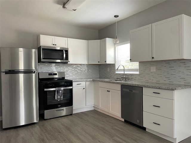 1701 40th St, Galveston, TX 77550 - kitchen with stainless steel appliances, a sink, white cabinets, light stone counters, and wood finished floors