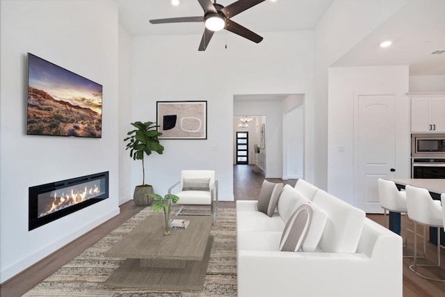 living room with a glass covered fireplace, recessed lighting, ceiling fan with notable chandelier, and wood finished floors
