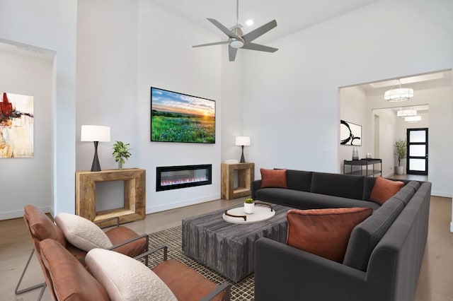 living area with baseboards, high vaulted ceiling, a glass covered fireplace, and a ceiling fan