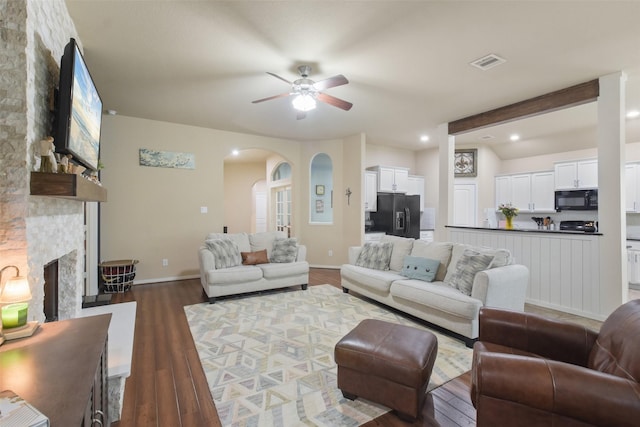 living area with a fireplace, dark wood-type flooring, arched walkways, a ceiling fan, and visible vents