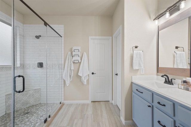 bathroom with a stall shower, wood finished floors, vanity, and baseboards