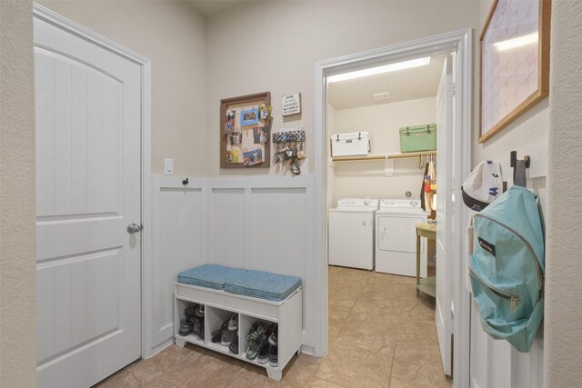 mudroom with a decorative wall, wainscoting, washing machine and clothes dryer, and light tile patterned flooring