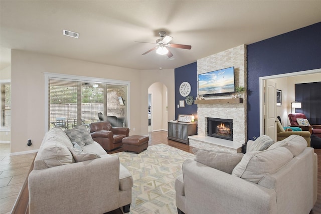 living area with a stone fireplace, baseboards, visible vents, ceiling fan, and arched walkways