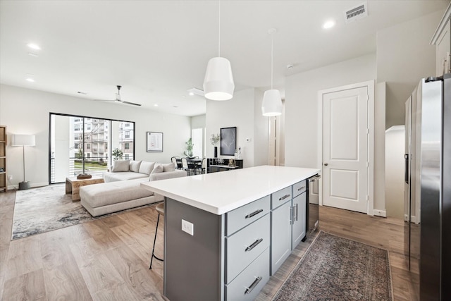 kitchen with a kitchen breakfast bar, gray cabinets, a center island, wood finished floors, and stainless steel fridge